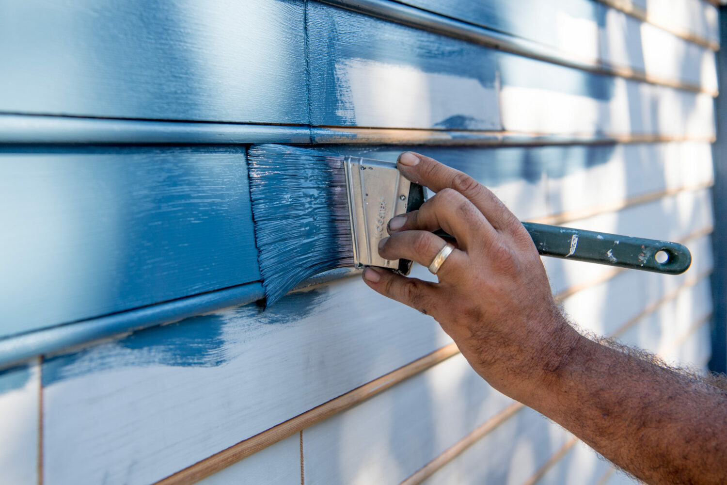 A hand is shown painting a bright blue on a historic house's shingles.