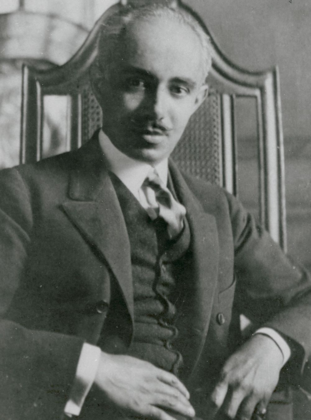Julian Abele seated in a wooden arm chair. He is wearing a jacket, waistcoat, and has a tie.